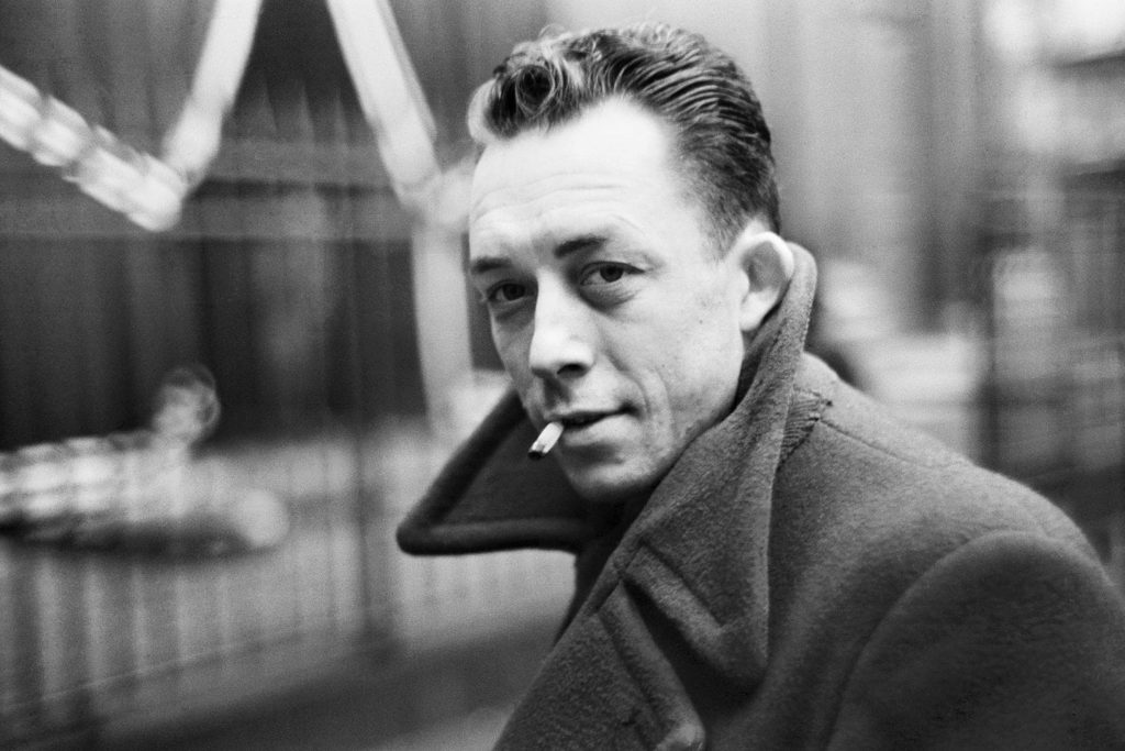 On voit Albert Camus en train de fumer une cigarette.